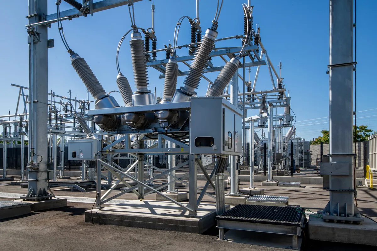 Outdoor electrical substation with high-voltage switchgear, transformers and insulators under a clear blue sky