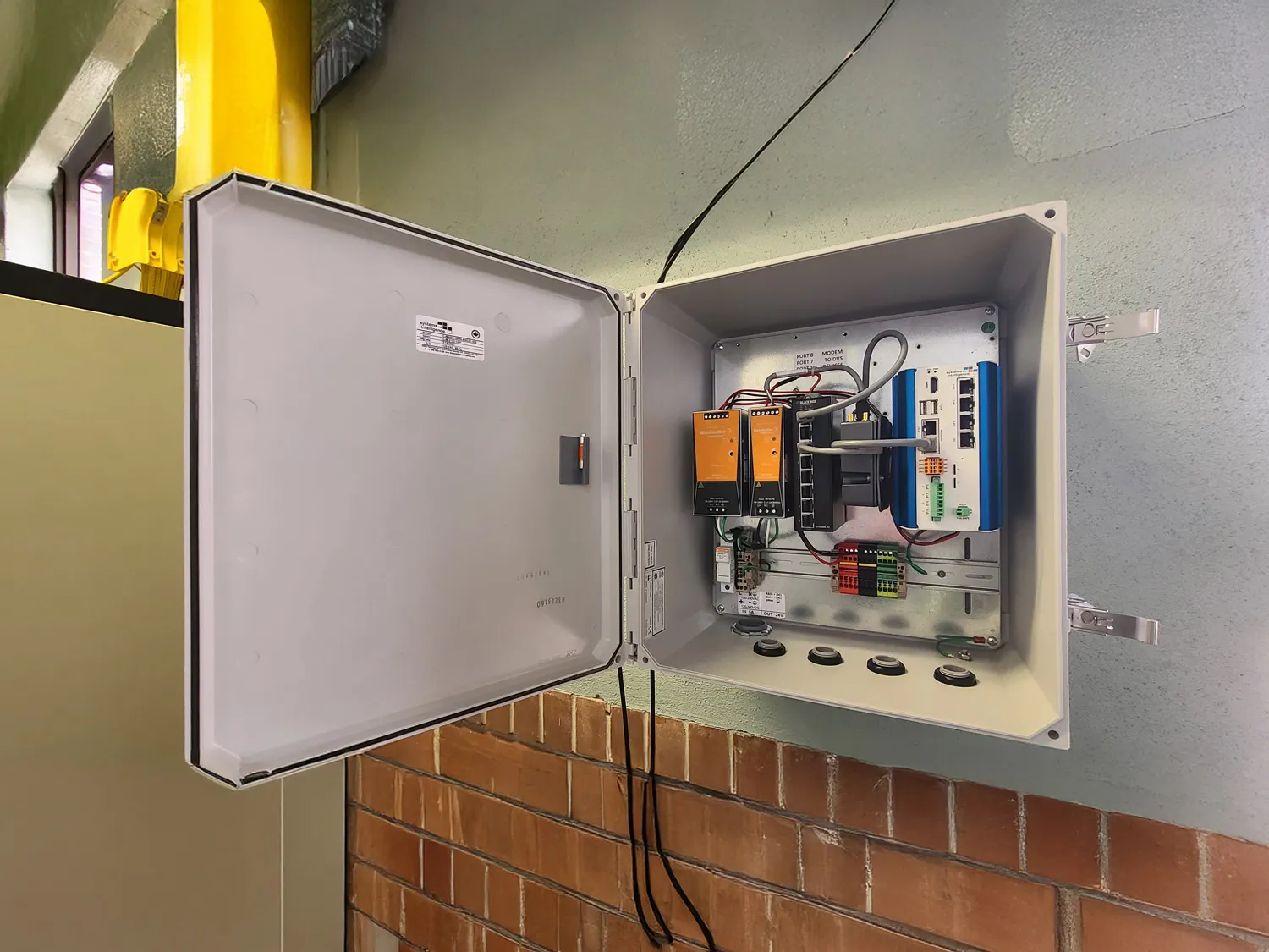 Open electrical control panel with orange modules, blue power supply and wiring mounted on a brick wall